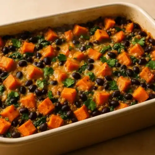 Baked sweet potato quinoa casserole in a cream ceramic dish with black beans, spinach, and melted cheese, garnished with cilantro.