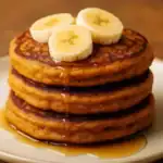 Close-up of fluffy vegan sweet potato pancakes topped with banana slices and drizzled with maple syrup.