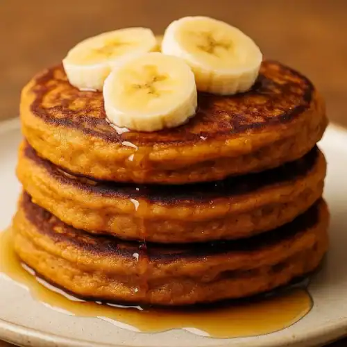 Close-up of fluffy vegan sweet potato pancakes topped with banana slices and drizzled with maple syrup.