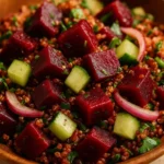 Close-up of a cold beet quinoa salad showing diced roasted beets, cucumber, red onion, parsley, and quinoa in a wooden bowl under warm lighting.