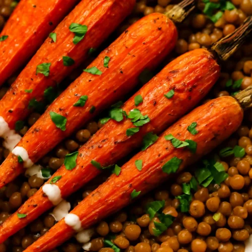 Close-up of roasted carrots with spiced lentils, topped with fresh parsley and a light tahini drizzle.