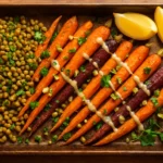 Sheet pan of roasted rainbow carrots with spiced lentils, tahini drizzle, parsley, pistachios, and lemon wedges on a warm wooden surface.